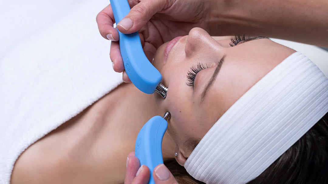 Person receiving a facial treatment with blue handheld tools on a white background